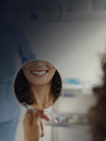 Foto de um espelho de mão refletindo uma boca sorrindo