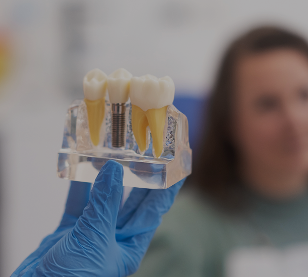 Imagem de um paciente desfocado, olhando para um modelo explicativo com prótese e implante